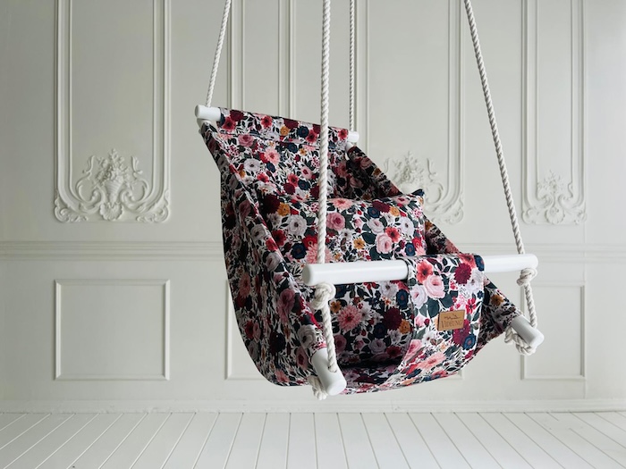 hostang-babygunga-hangande Handtillverkad babygunga Höstäng med tätt höstblommönster, hängande i bomullsrep mot vit vägg. Handmålade träpinnar och Videung-logga.
